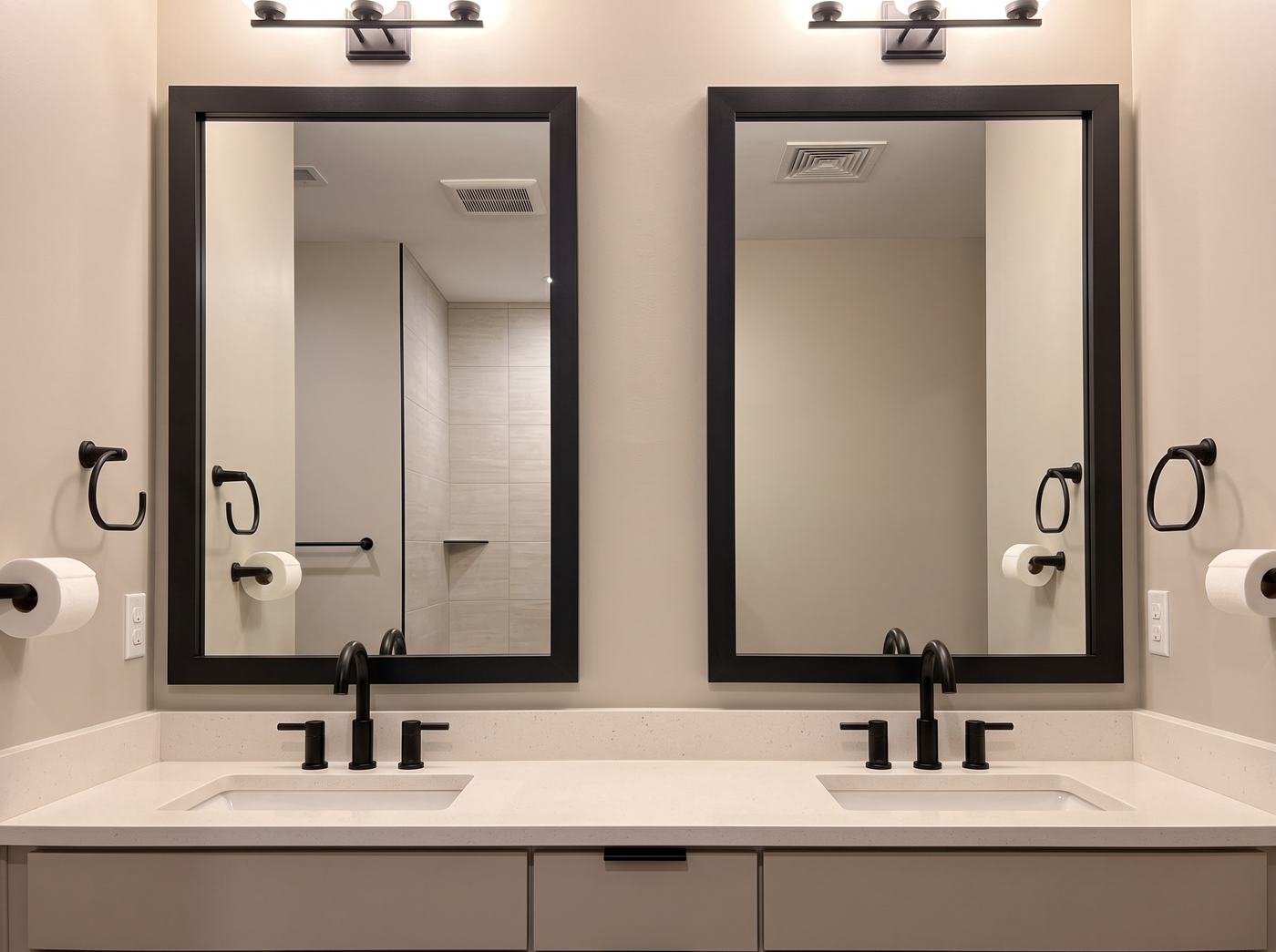 A modern double-sink bathroom vanity with two large black-framed mirrors, matte black faucets, white countertops, and matching black wall-mounted toilet paper holders.